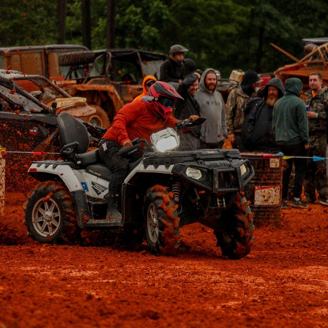 Red rain jacket ATV rider in deep mud with a crowd of spectators watching.