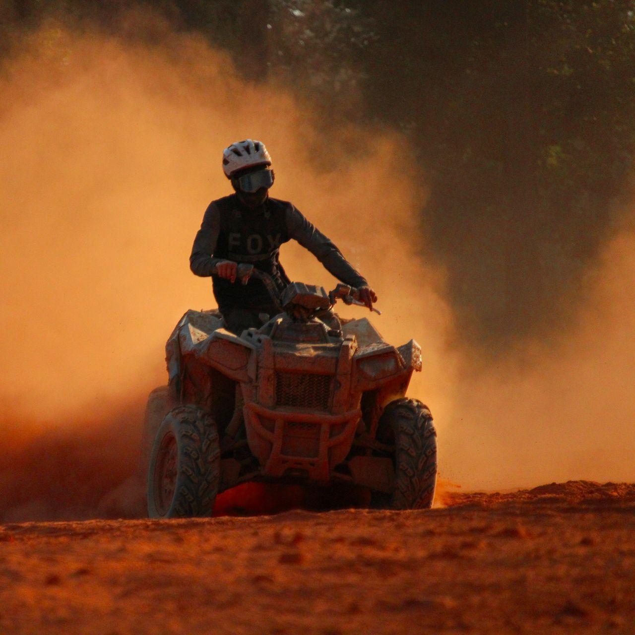 Solo ATV rider in Fox jersey kicking up orange dust at sundown.