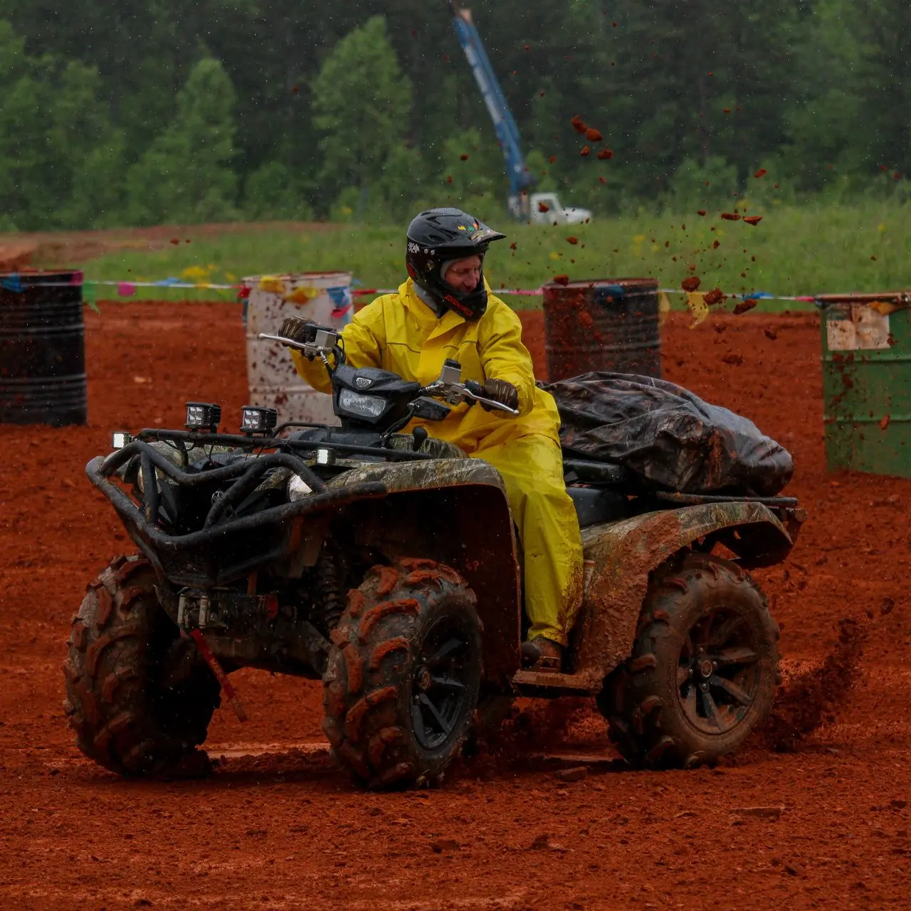 ATV in yellow rain suit kicking red clay chunks during a barrel race.