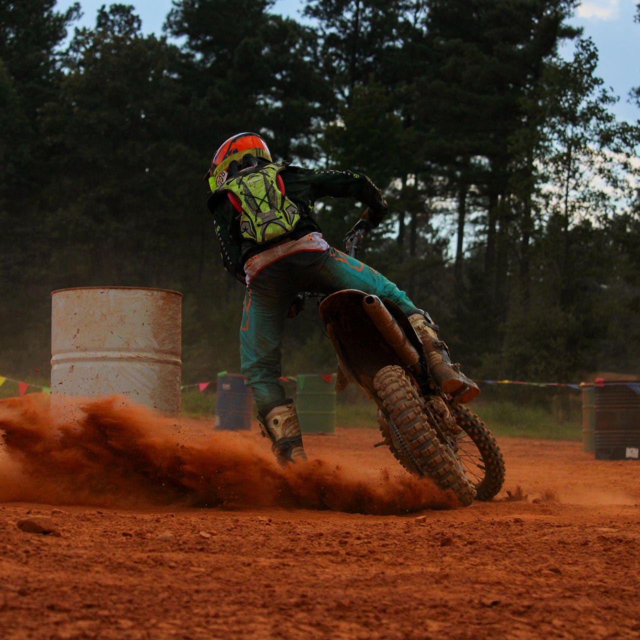 Dirt bike sliding tight around a barrel in red clay.