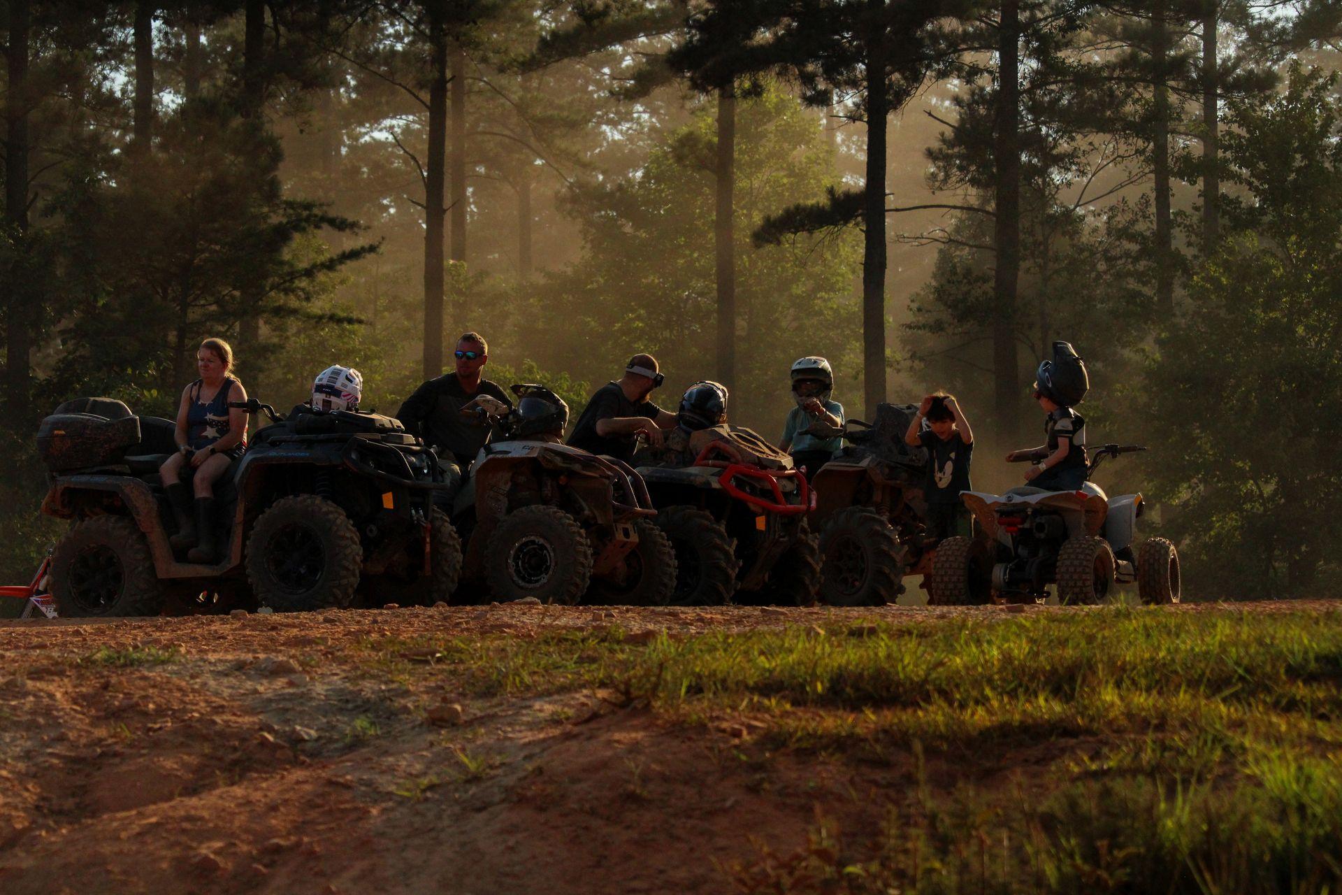 A group of ATV and UTV riders parked in a line under pine trees at Iron Mountain Resort at golden hour.